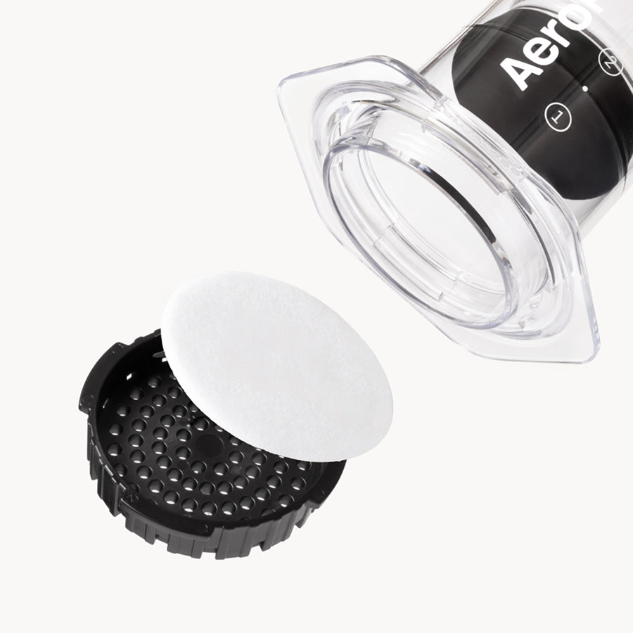 Placering av ett AeroPress pappersfilter i det svarta filterlocket till en AeroPress Clear