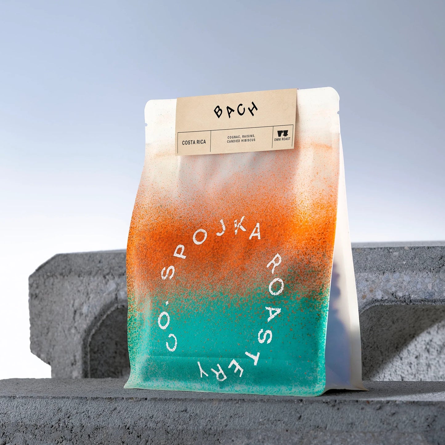 Gradient coffee bag with 'Spojka Roastery' branding on a concrete surface.