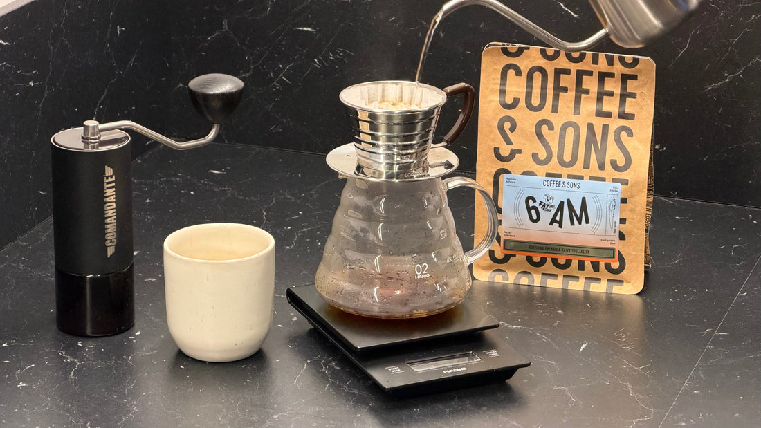 Manuell pour-over-tillredning med en Kalita Wave-dripper, glaskanna på en digital våg, en handkvarn och en påse Coffee & Sons 6AM-kaffe.