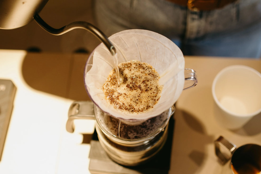 Hällning av varmt vatten från en vattenkokare över malet kaffe i en dripper.