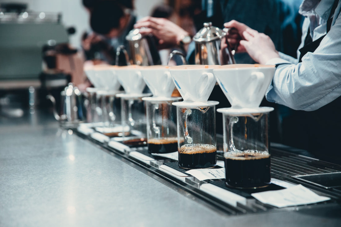 Baristor som tillreder flera pour-over-kaffe i rad på ett modernt café.