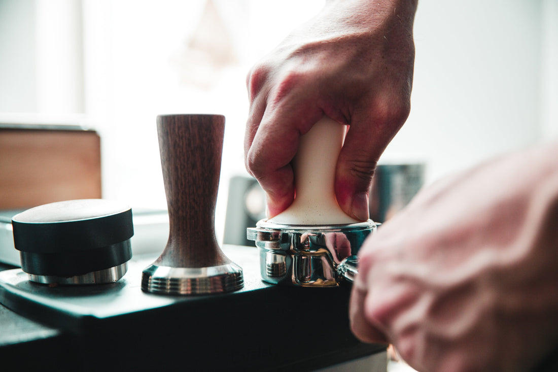Barista som pressar kaffe i portafiltret med en tamper.