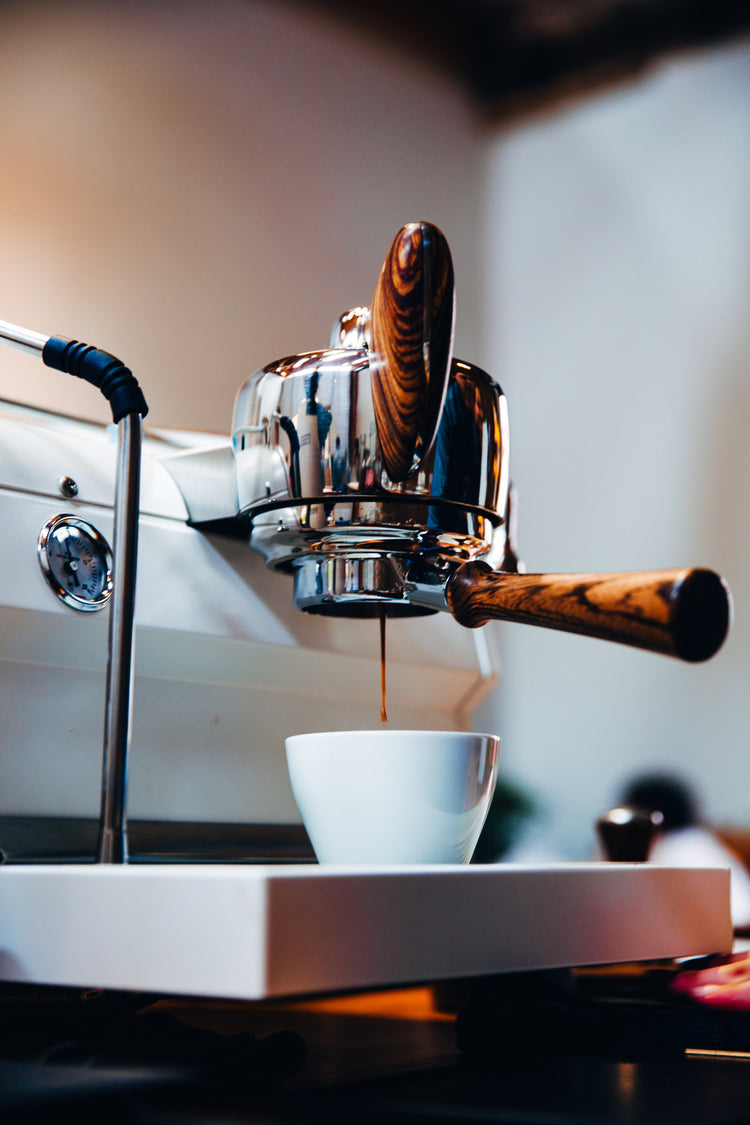 A high-end espresso machine with polished dark wood handles extracting a fresh shot of espresso into a white cup.