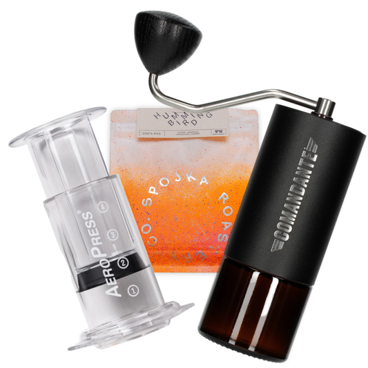 AeroPress Clear coffee maker, Comandante grinder, and orange coffee bag  on a white background