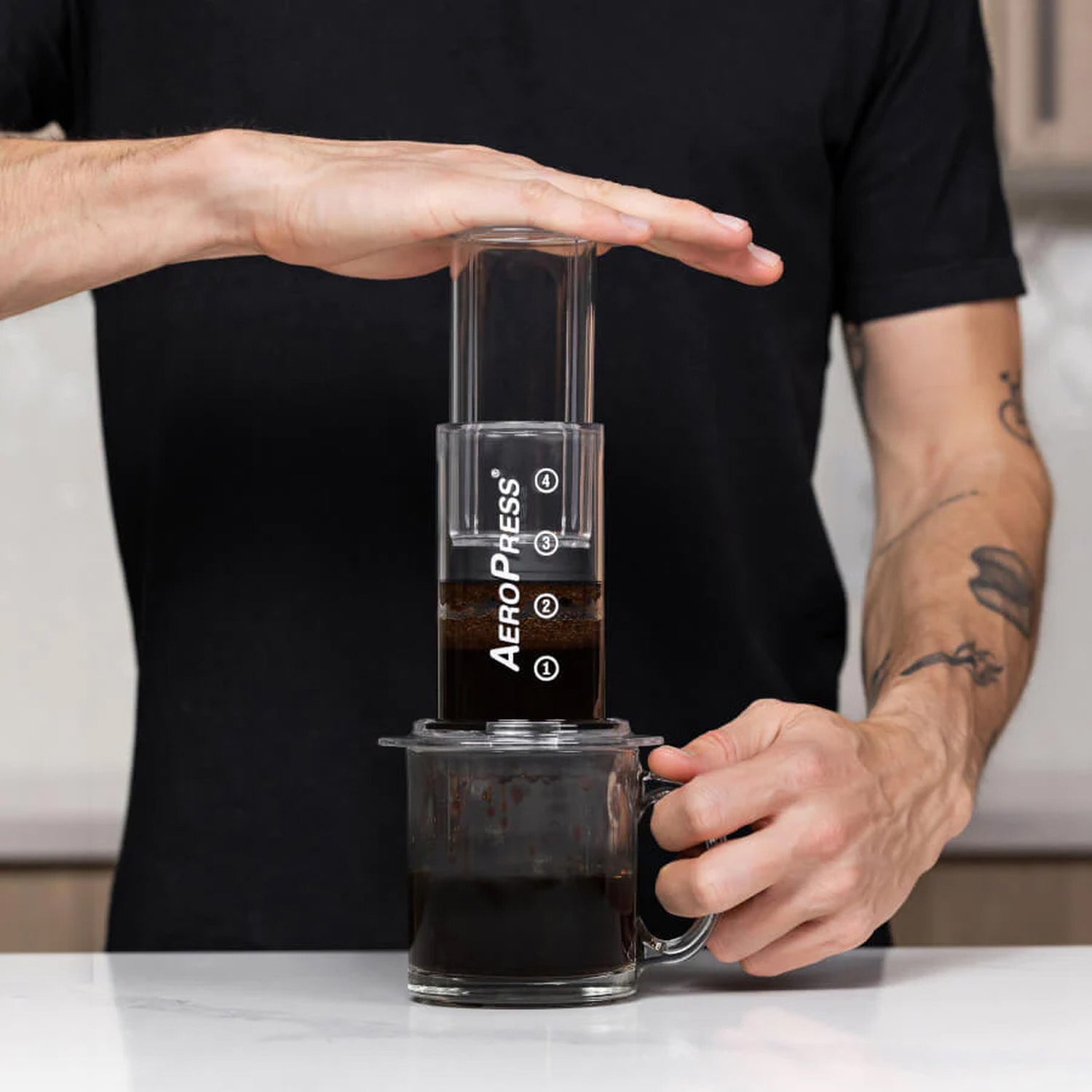En person som pressar ner en AeroPress Clear för att brygga kaffe i en glasmugg