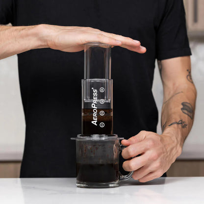 En person som pressar ner en AeroPress Clear för att brygga kaffe i en glasmugg