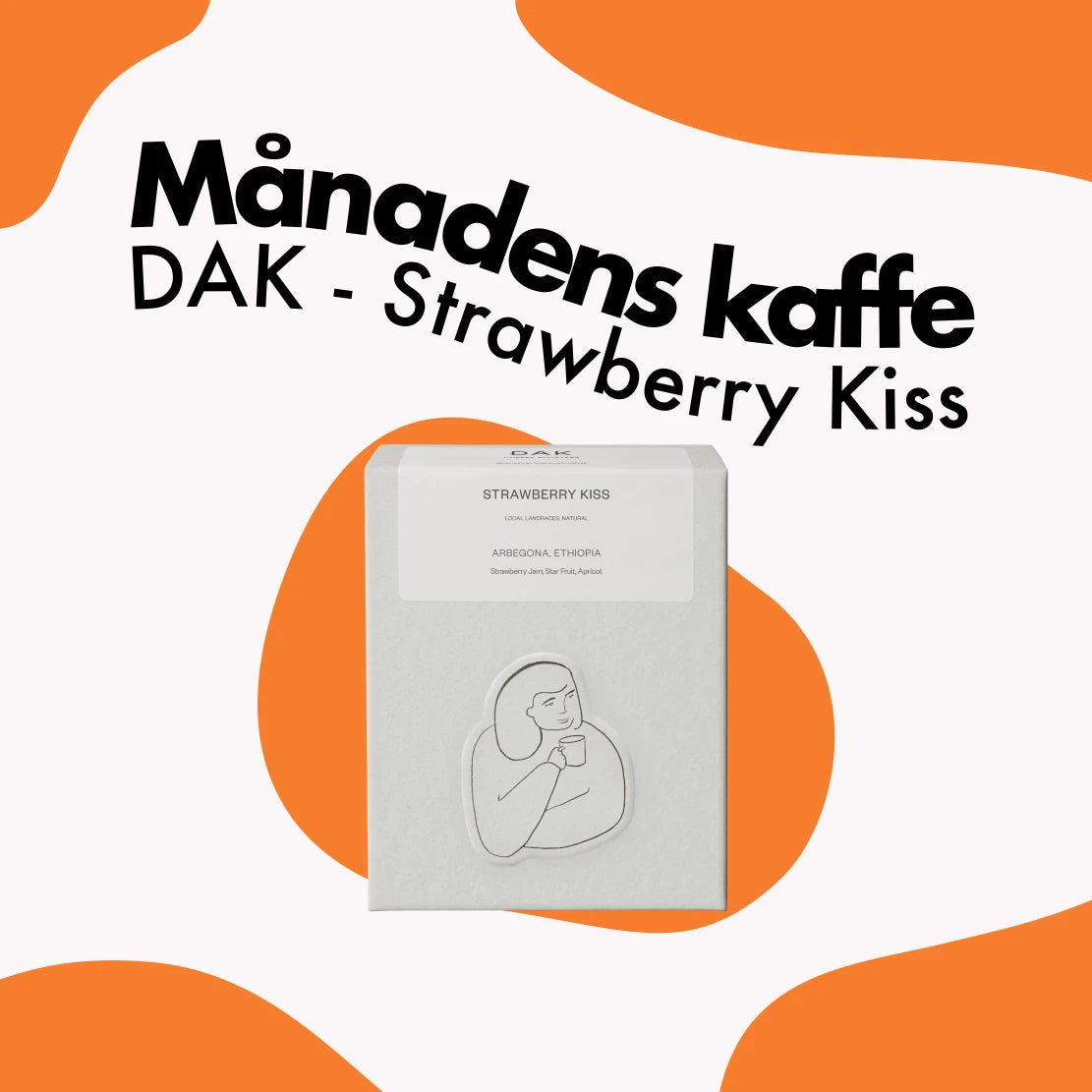 Kvadratisk banner för Månadens kaffe som visar en vit kartong DAK - Strawberry Kiss kaffe mot en vit och orange vågig bakgrund.