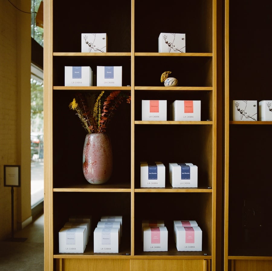Wooden retail shelves stocked with La Cabra coffee boxes and a decorative vase.
