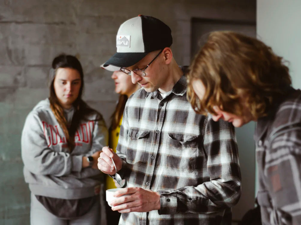 Group of people gathered around a person holding a container, with a focus on the central figure.
