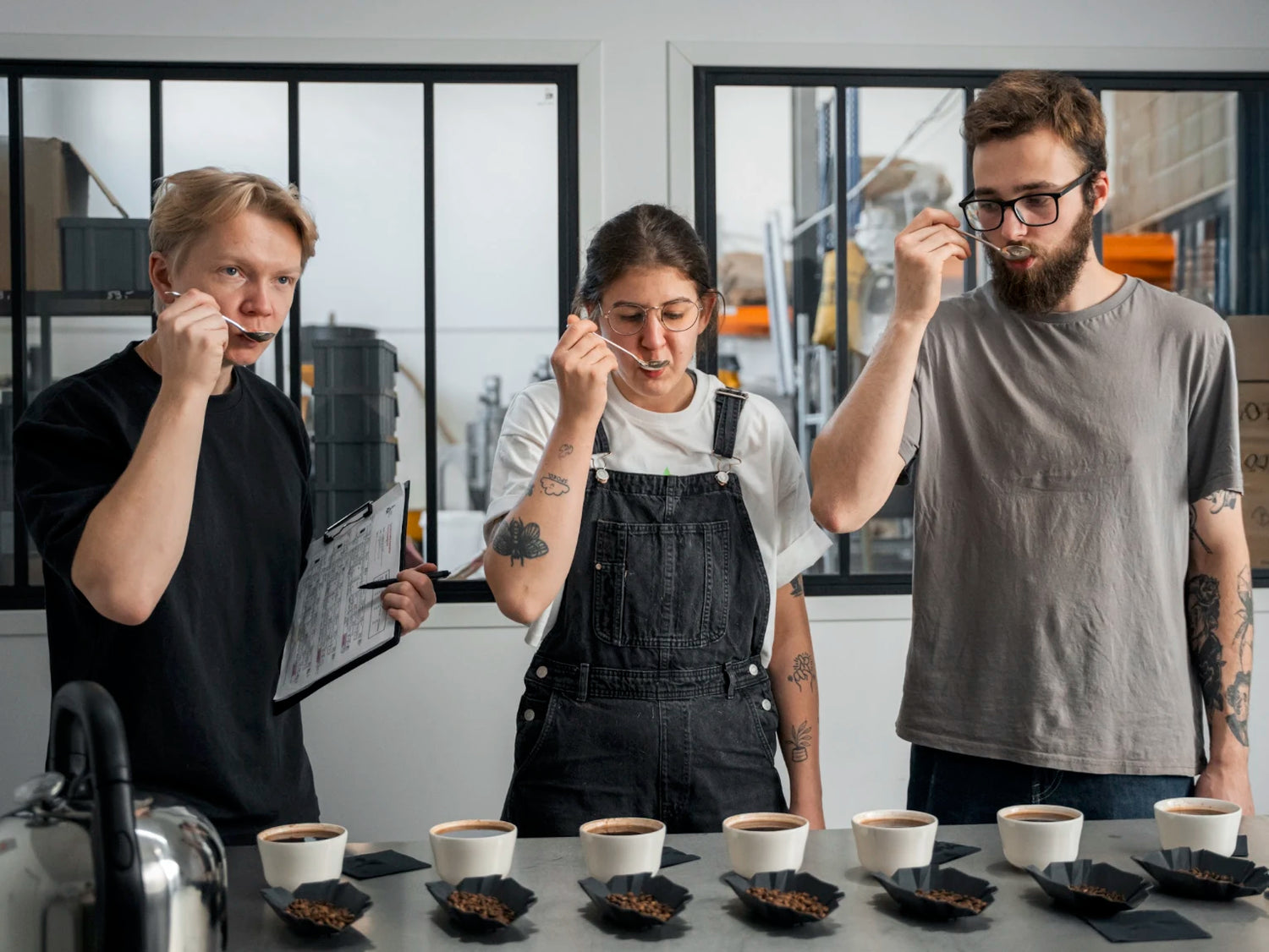 Three professionals tasting coffee with spoons during a quality control cupping session.