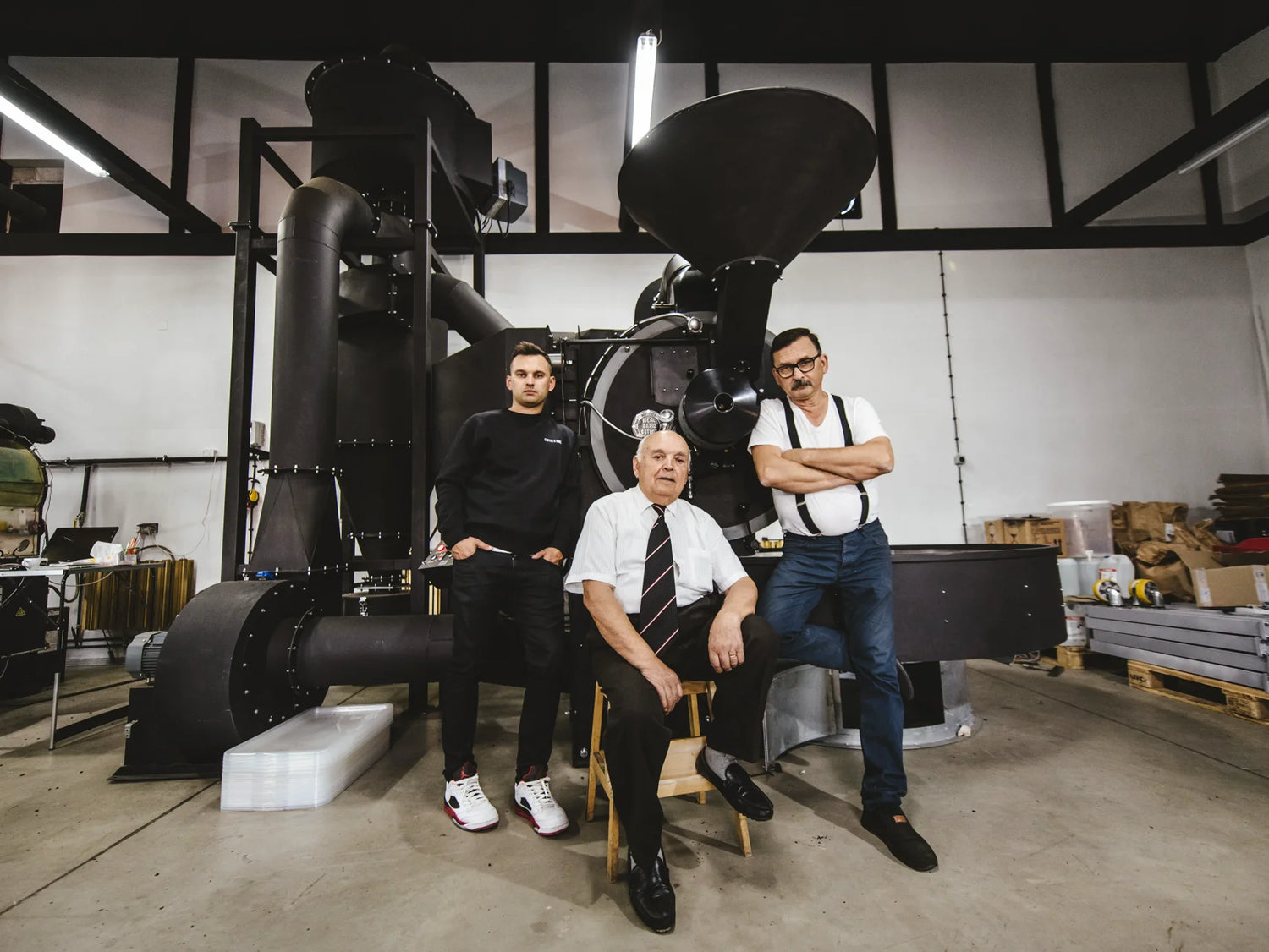 Three men posing in front of a large coffee roasting machine in a workshop setting.