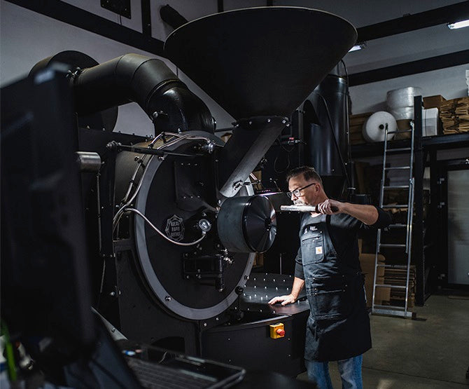 Person operating a large coffee roaster in a warehouse setting