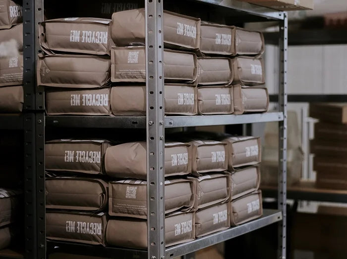 Stacks of brown bags labeled 'RECYCLE ME' on metal shelves in a warehouse setting.