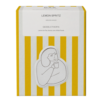 Gul och vit ask DAK Coffee Roasters Colombia Lemon Spritz Filter hela bönor med guldritning på grön bakgrund av en person