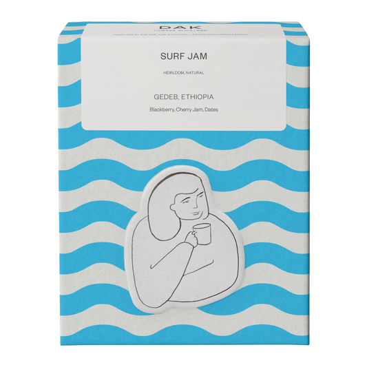 Blue and white wavy box of DAK Coffee Roasters Surf Jam Gedeb Ethiopia Whole Beans with a black outline drawing of a person holding a mug