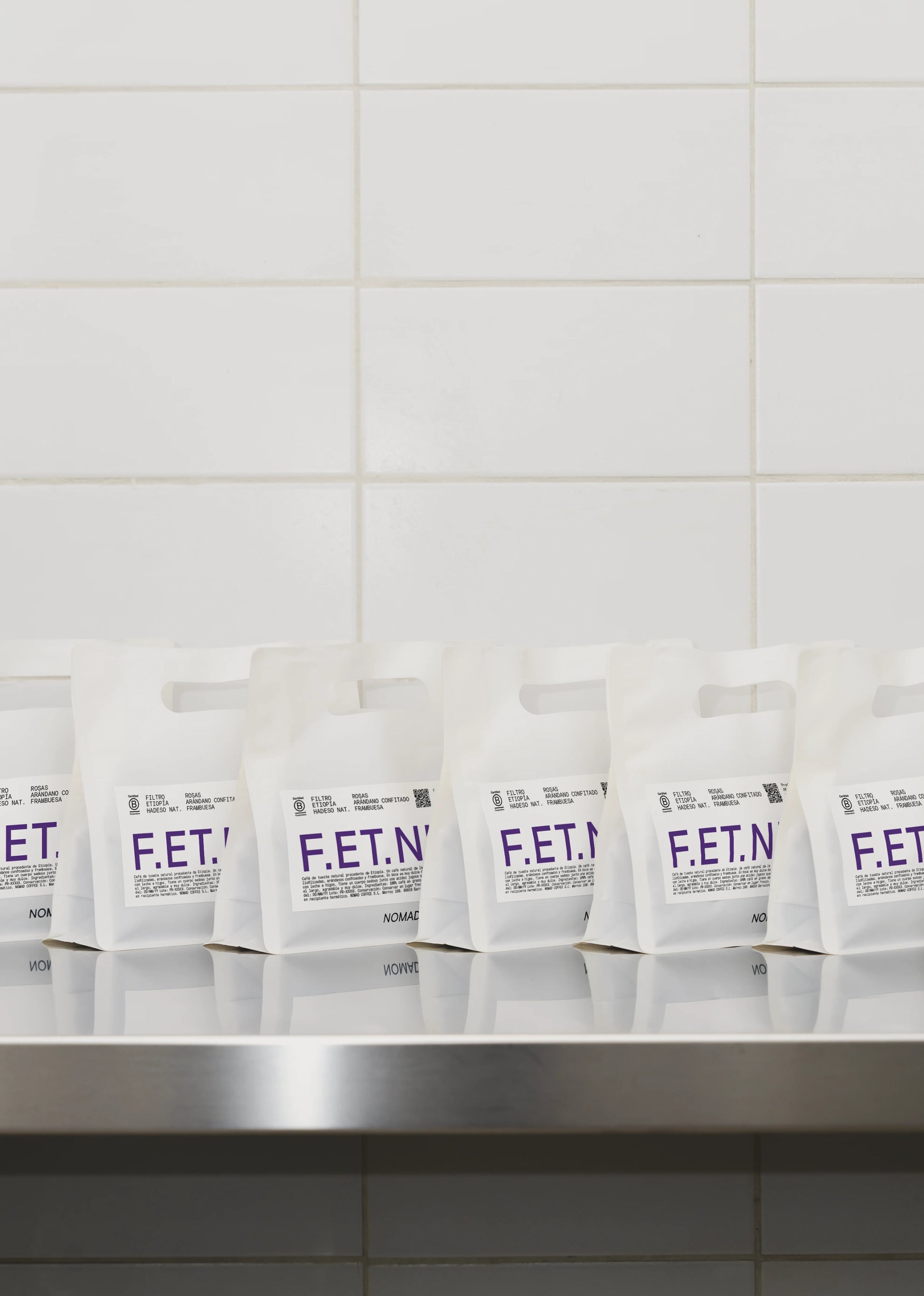 En rad vita kaffepåsar i plast från Nomad Coffee med lila och svart text som läser "F.ET."