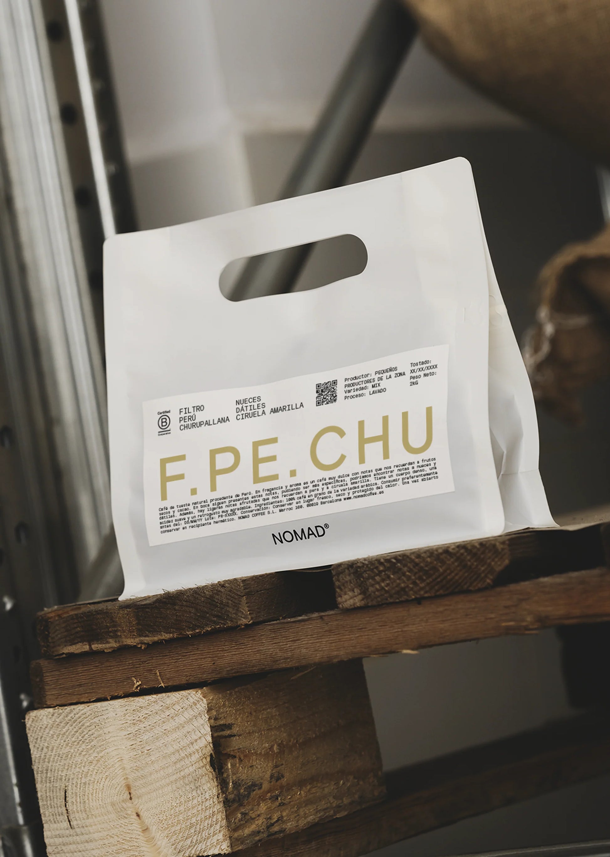 Vit kaffepåse i plast från Nomad Coffee med F.PE.CHU-etikett på en träyta