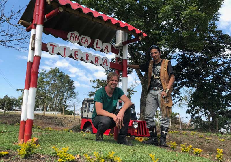 Two people posing in front of a sign reading 'Finca La Tierra' with a red and white structure.