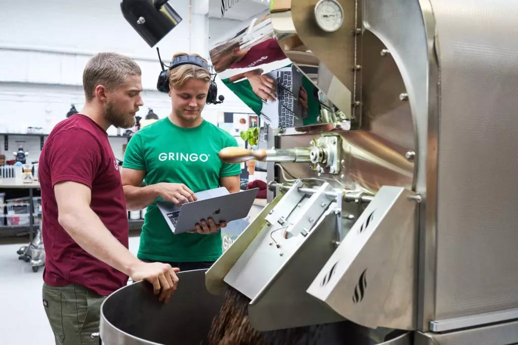 Two men working with a coffee roasting machine in a factory setting.