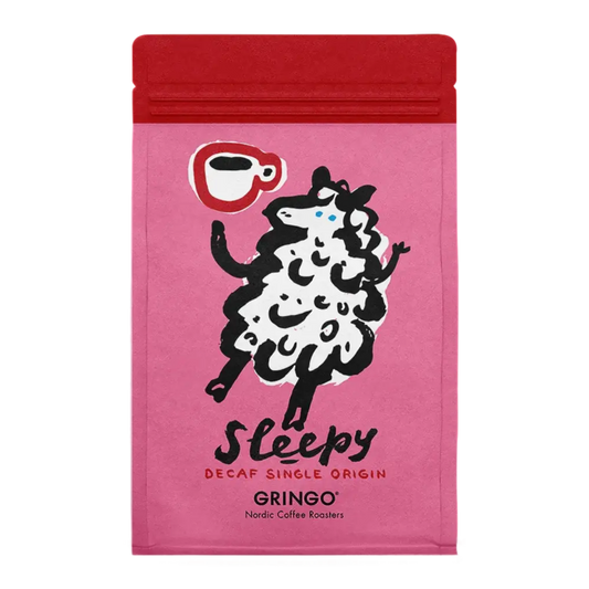 A bright pink coffee bag for "Sleepy" Decaf Single Origin by Gringo Nordic Coffee Roasters. It features a whimsical illustration of a white sheep holding a red coffee cup.