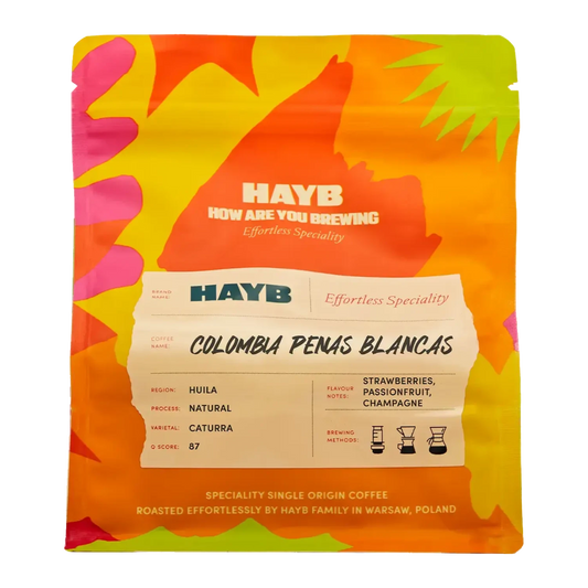 En påse HAYB Colombia Penas Blancas specialkaffe med en färgstark abstrakt design i orange och gult.