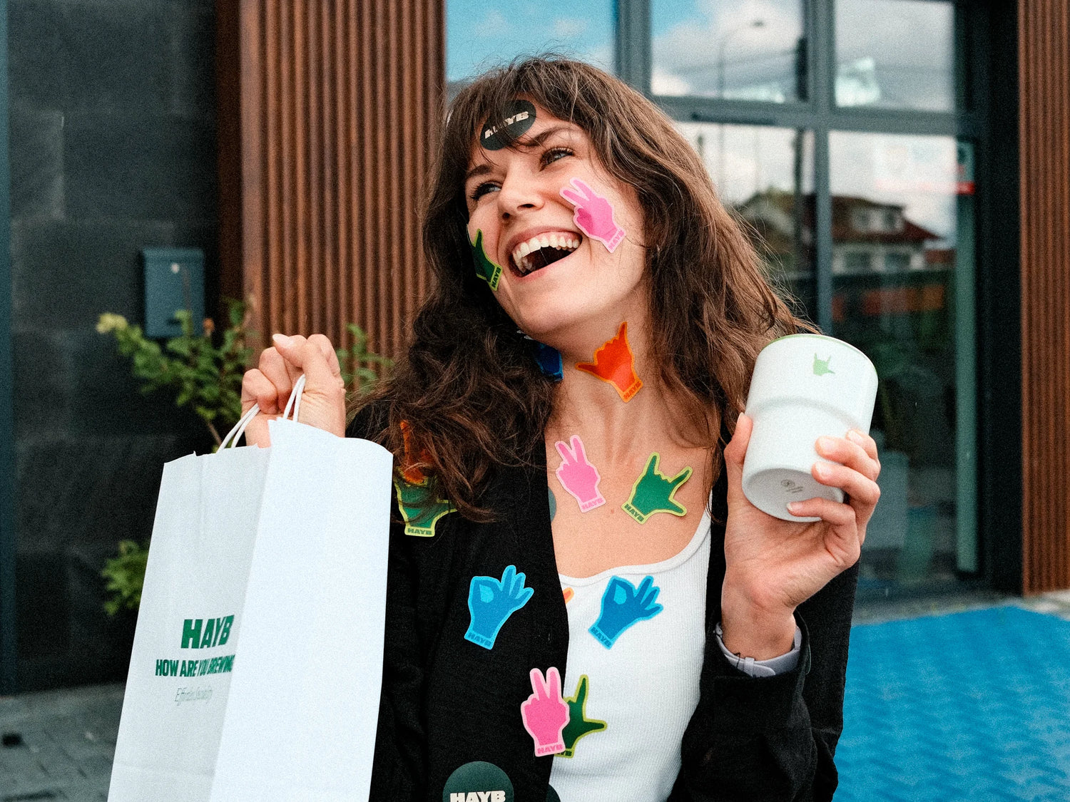 Woman with colorful stickers holding a cup and shopping bag and mug outdoors.