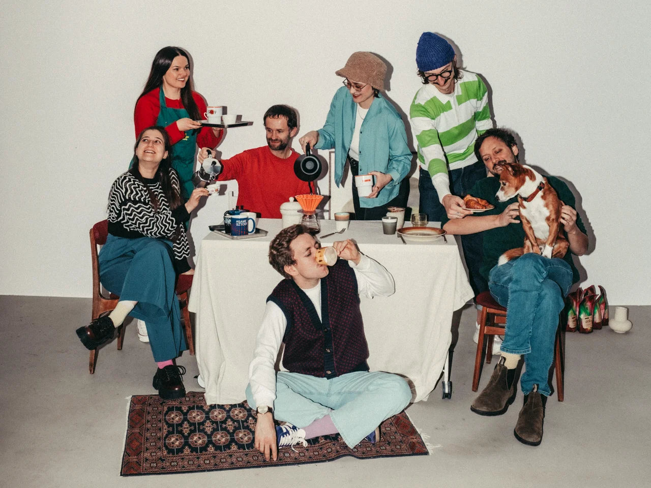Group of people sitting around a table with a dog, posing for a photo.