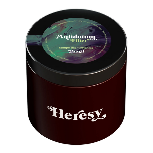 En mörkröd cylindrisk burk med svart lock som visar en "Heresy"-logotyp och en färgglad "Antidotum" filterkaffeetikett.
