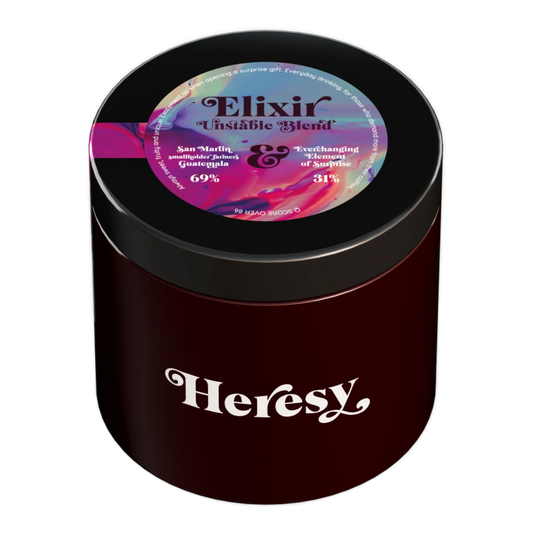 En mörkröd cylindrisk burk med svart lock som visar en "Heresy"-logotyp och en färgglad toppetikett för "Elixir UnstableBlend".