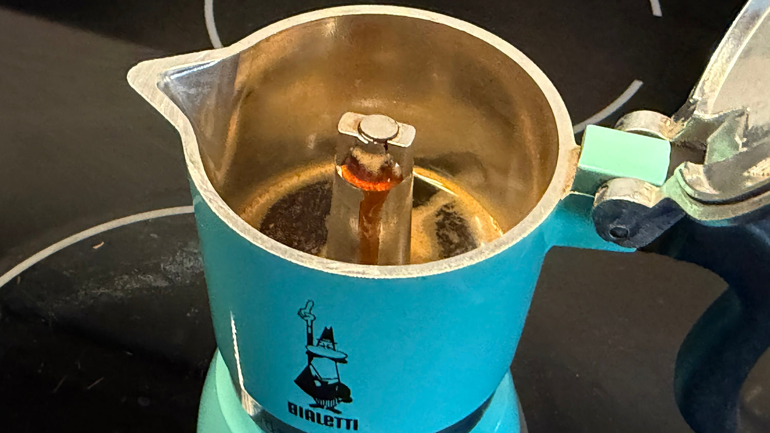 Blue Bialetti coffee maker with coffee brewing inside on a dark surface