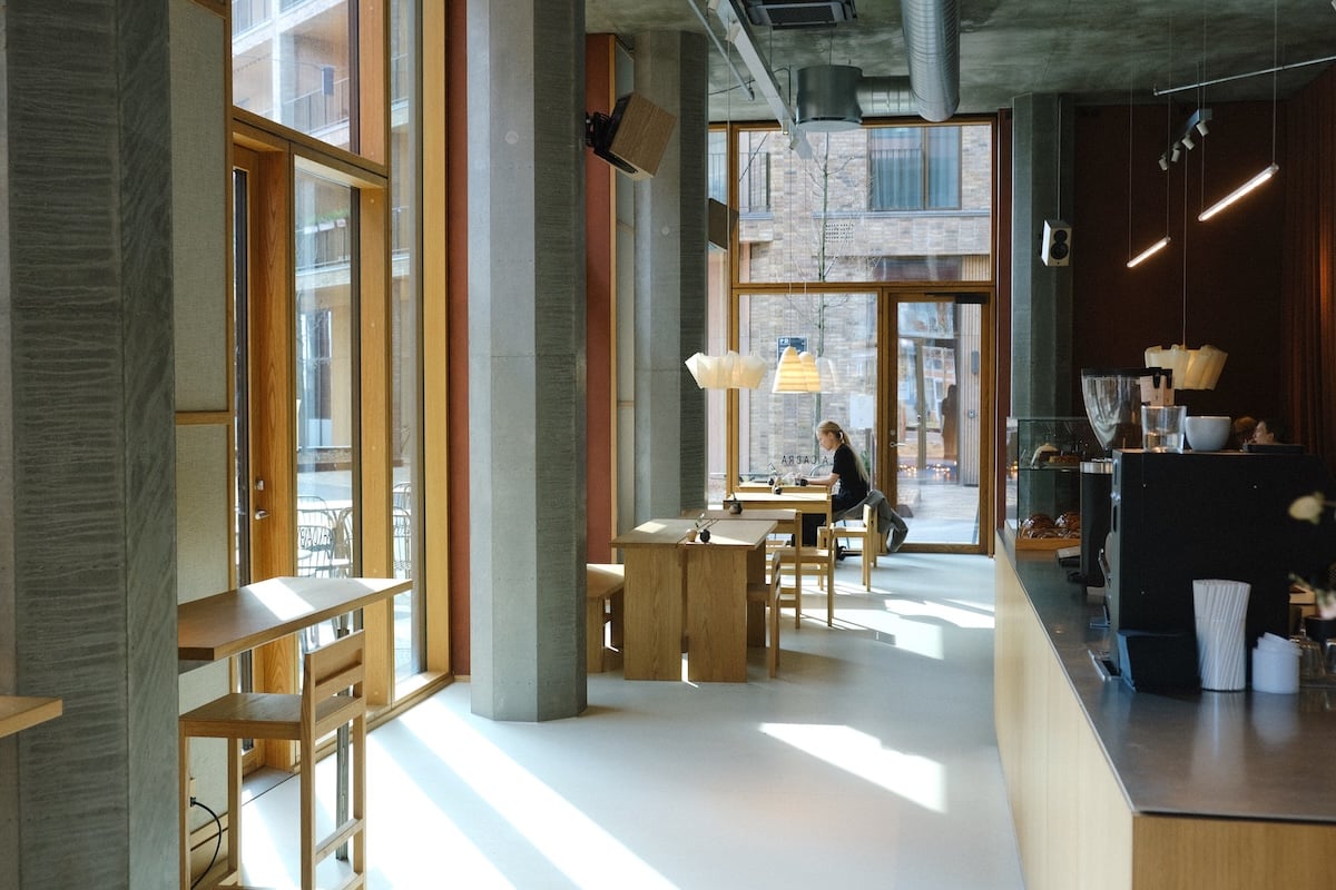 Bright modern interior of La Cabra coffee bar with wooden tables and concrete pillars.