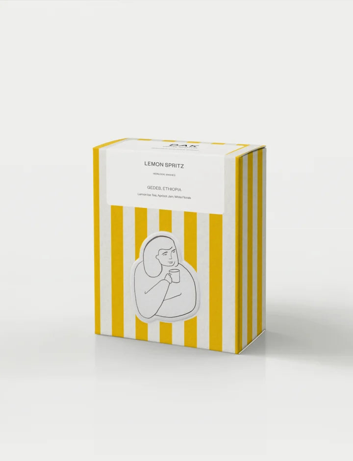 Gul- och vitrandig kaffelåda från DAK Coffee Roasters med texten "Lemon Spritz" på vit bakgrund