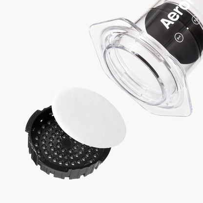 Placing an AeroPress paper filter into the black filter cap of a clear AeroPress.