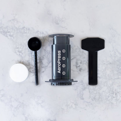 AeroPress Original set med pappersfilter, måttskopa och omrörare på en marmoryta