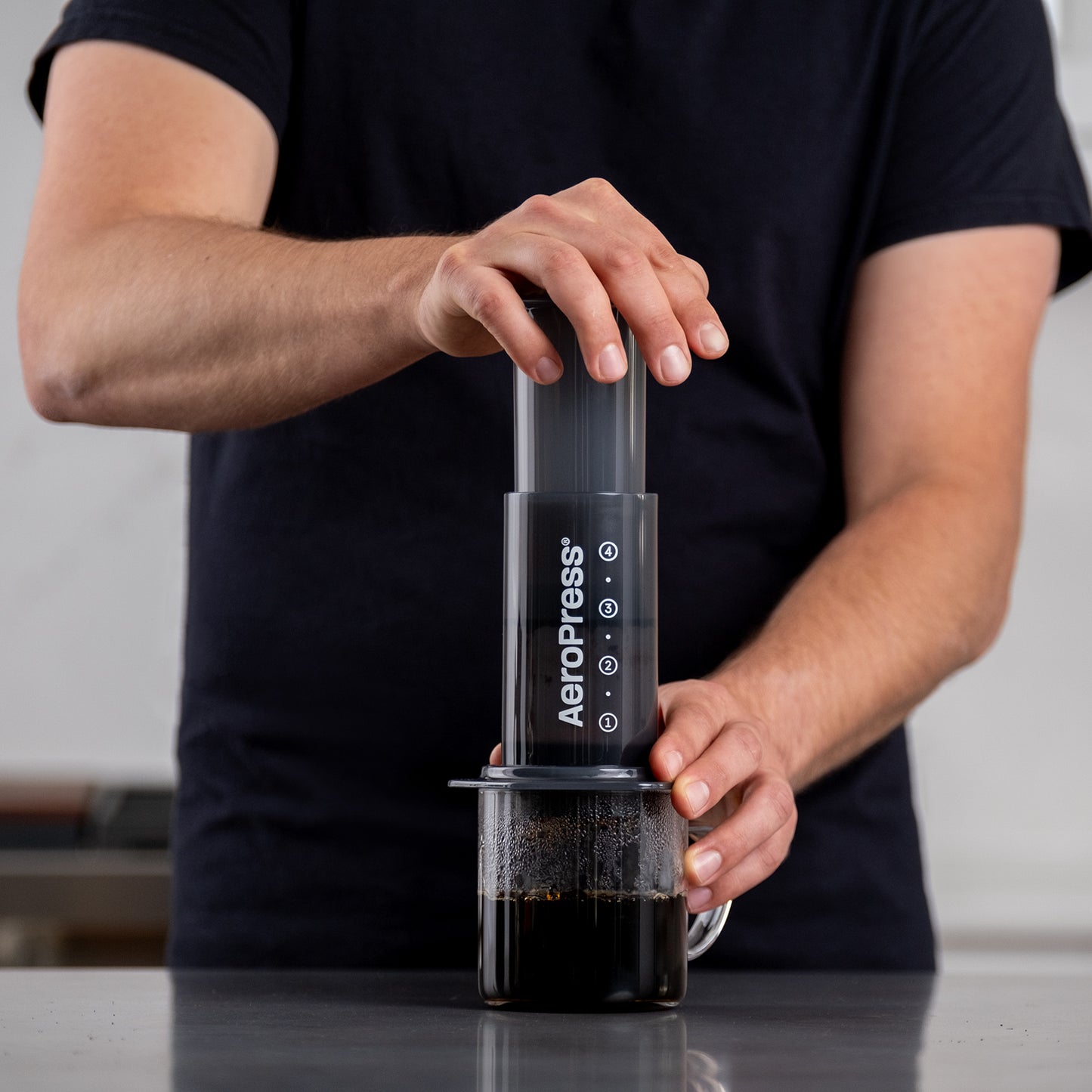 Hand som pressar AeroPress Original kaffebryggare över en genomskinlig mugg