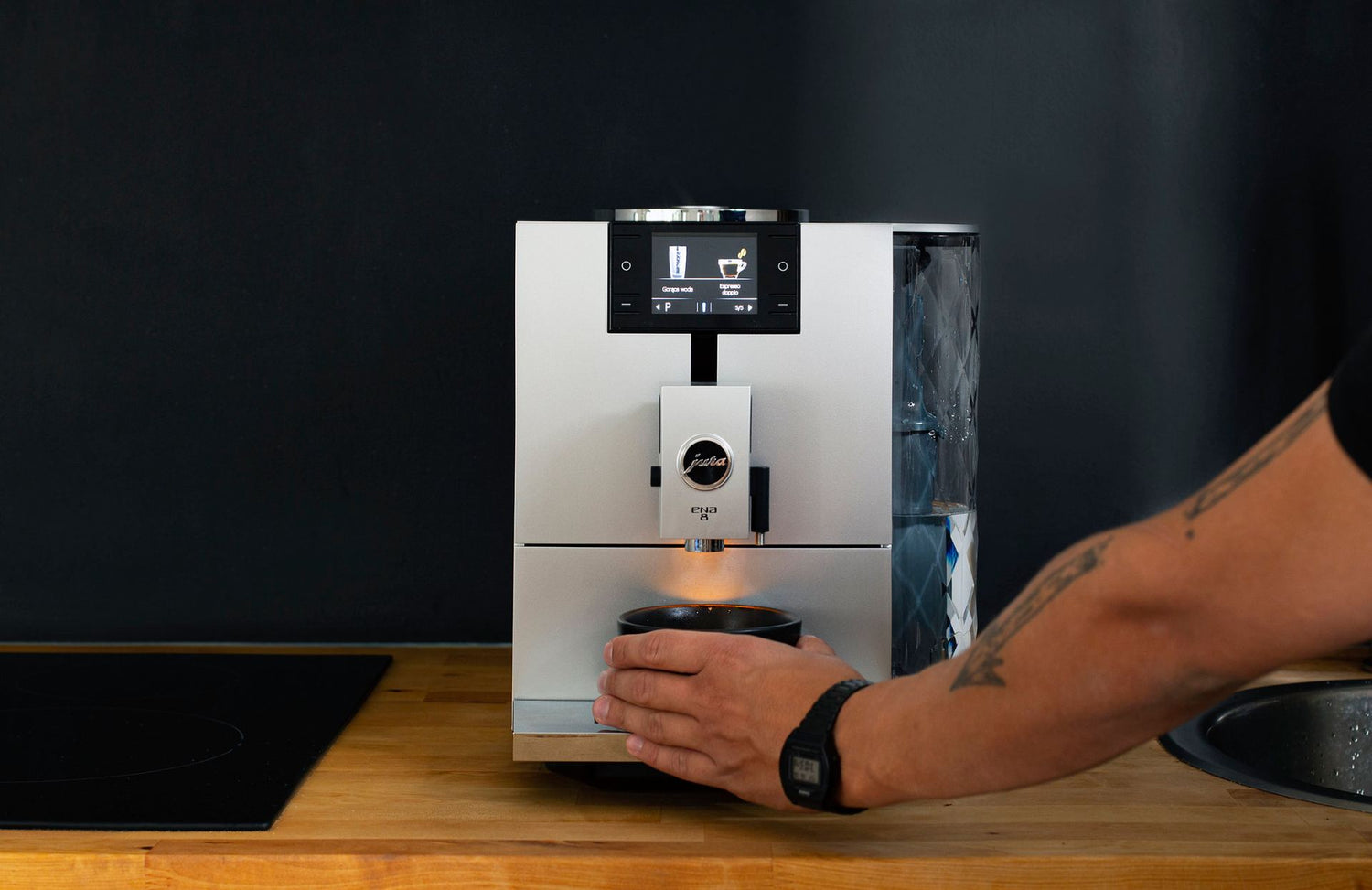 En person som ställer en kopp under en Jura automatisk espressomaskin.