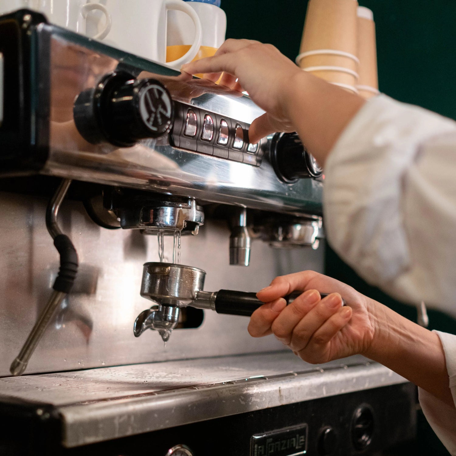 A close-up of a barista operating an espresso machine, adjusting the controls and holding a portafilter. 