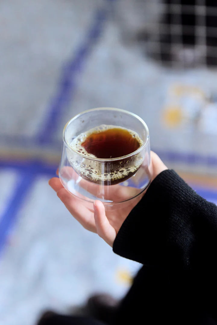 Hand holding a double-walled glass cup filled with brewed black coffee