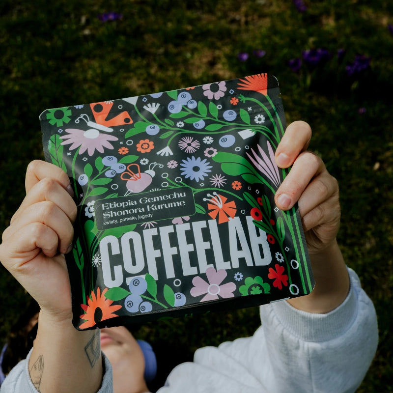 Person som håller en färgglad CoffeeLab-förpackning mot en naturlig bakgrund.