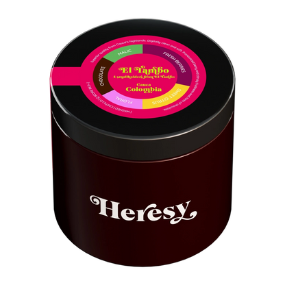 En mörkröd cylindrisk burk med svart lock som visar en "Heresy"-logotyp och en färgglad toppetikett för "El Tambo".