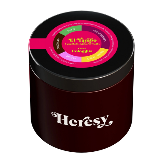 En mörkröd cylindrisk burk med svart lock som visar en "Heresy"-logotyp och en färgglad toppetikett för "El Tambo".