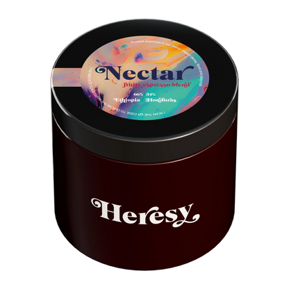 En mörkröd cylindrisk burk med svart lock som visar en "Heresy"-logotyp och en färgglad toppetikett för "Nectar" espressoblend.