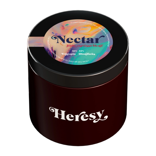 En mörkröd cylindrisk burk med svart lock som visar en "Heresy"-logotyp och en färgglad toppetikett för "Nectar" espressoblend.