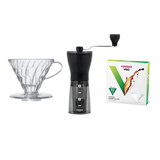Hario coffee brewing set with grinder, filter, and clear Hario V60-02 filters on a white background