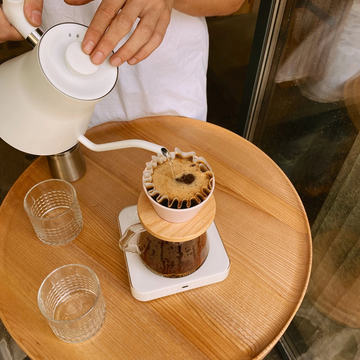 Person making coffee using a pour-over method on a wooden table.