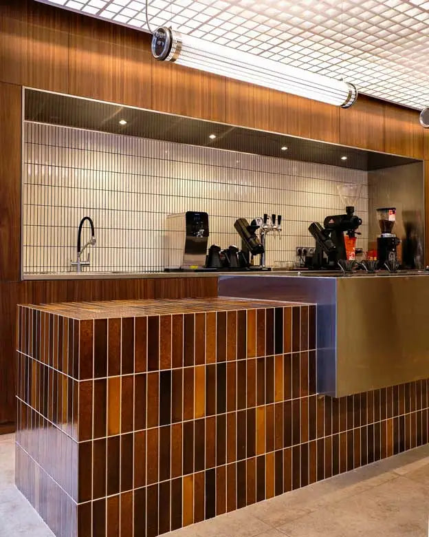 A modern bar or cafe counter with a wood and metallic tile design, featuring a tiled backsplash and coffee equipment.