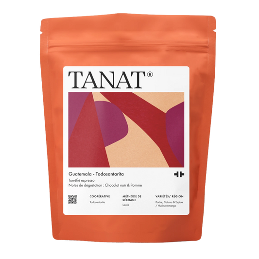 En stående påse med TANAT Guatemala - Todosantarita kaffebönor, med en klarorange kropp med en vit etikett som innehåller mångfärgade abstrakta former.